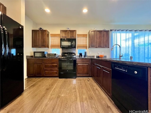 kitchen with light wood-type flooring, black appliances, dark countertops, and a sink