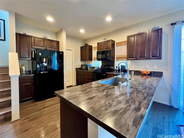 kitchen with dark countertops, black appliances, a peninsula, and a sink