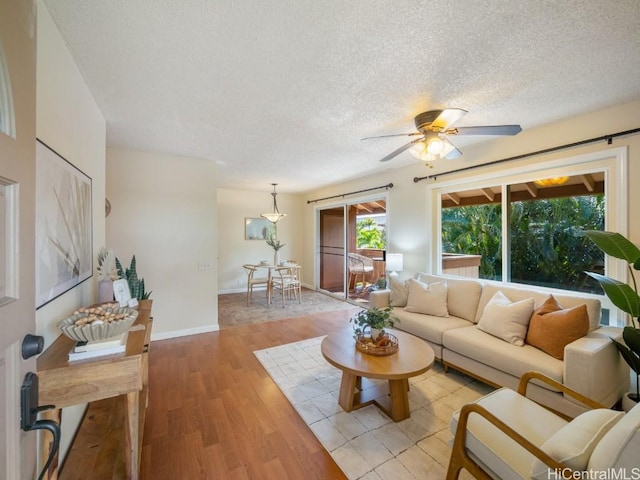 living room with a textured ceiling, ceiling fan, light wood-style flooring, and baseboards