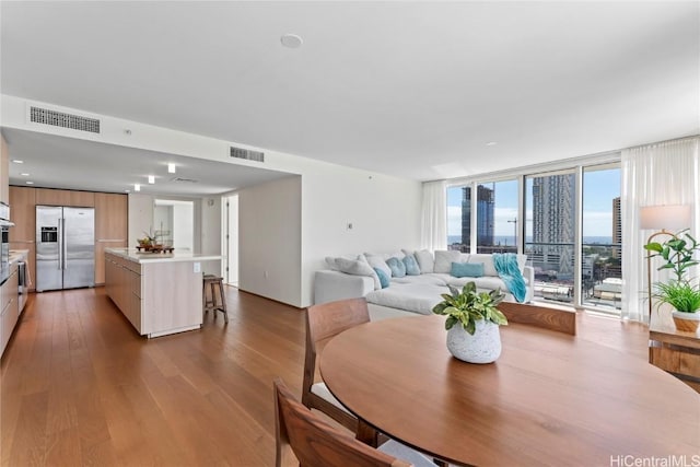 dining room with a view of city, light wood-style flooring, a wall of windows, and visible vents