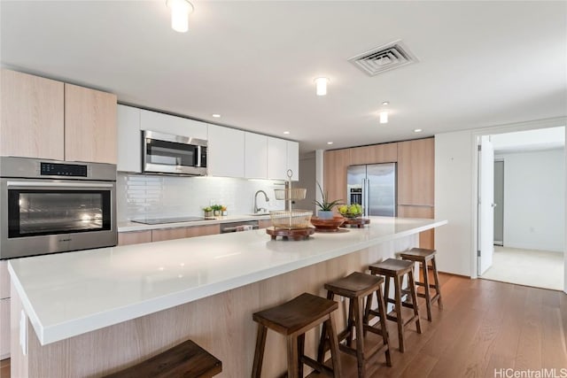 kitchen featuring stainless steel appliances, visible vents, white cabinets, a kitchen breakfast bar, and light countertops