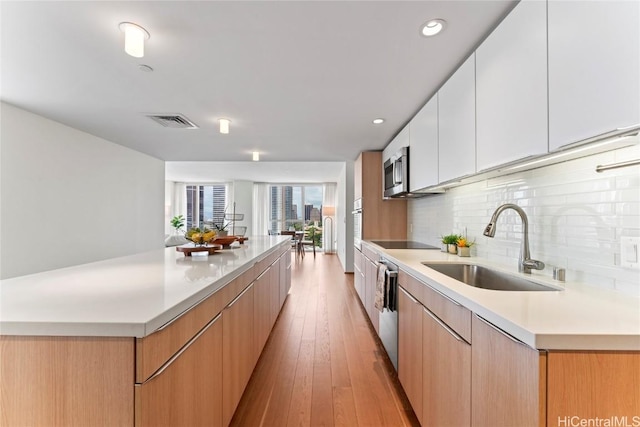 kitchen featuring light countertops, stainless steel microwave, white cabinets, a sink, and modern cabinets