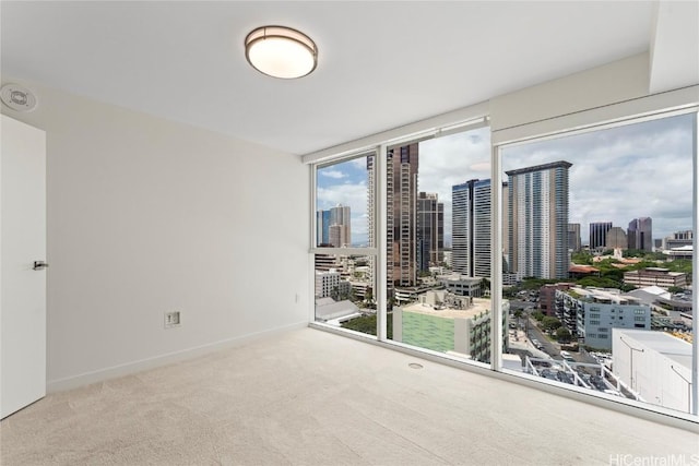 empty room featuring a view of city, baseboards, a wall of windows, and light colored carpet