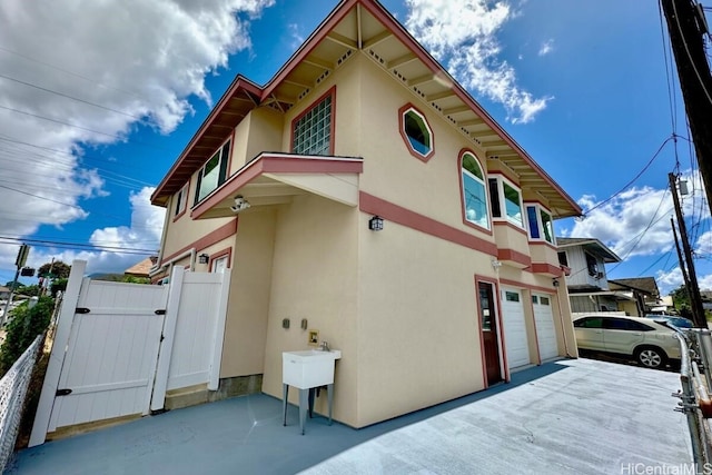 view of side of property with a garage, fence, a gate, and stucco siding