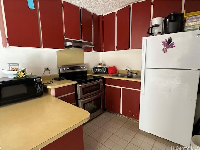 kitchen with black microwave, under cabinet range hood, red cabinets, freestanding refrigerator, and double oven range