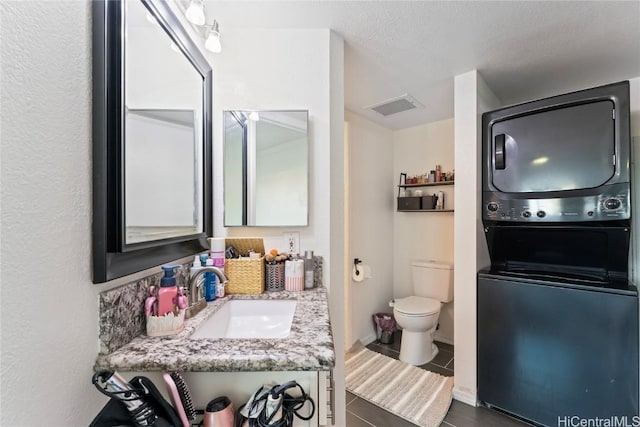 bathroom with toilet, visible vents, stacked washer / drying machine, and vanity