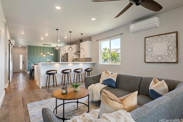 living room featuring ceiling fan, a wall unit AC, recessed lighting, baseboards, and light wood finished floors