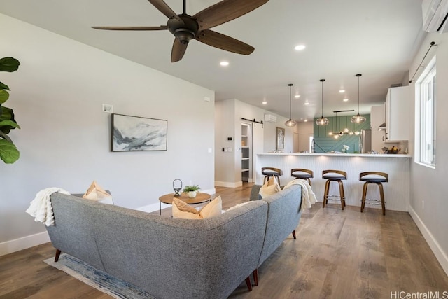 living area featuring a barn door, baseboards, dark wood finished floors, a wall unit AC, and recessed lighting