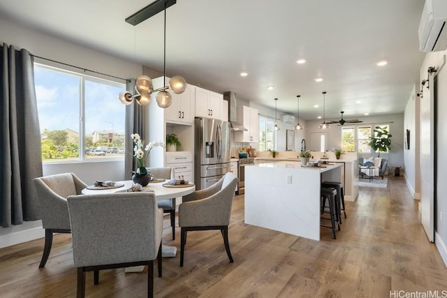 kitchen with white cabinets, a wall unit AC, appliances with stainless steel finishes, wall chimney range hood, and pendant lighting