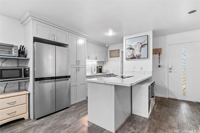 kitchen with appliances with stainless steel finishes, dark wood finished floors, a peninsula, and a sink