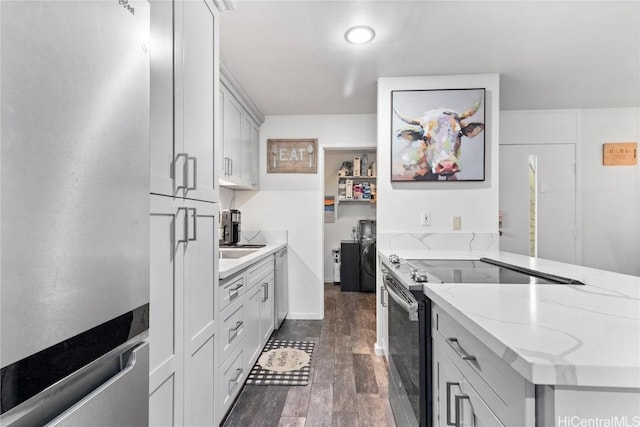 kitchen with stainless steel appliances, dark wood-type flooring, a peninsula, and light stone countertops