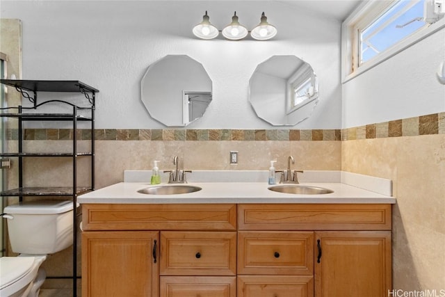 bathroom featuring a sink, tile walls, toilet, and double vanity