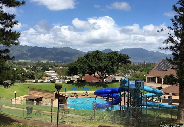 view of property's community featuring playground community, a mountain view, a lawn, and fence