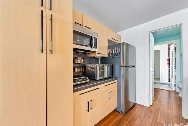 kitchen with dark countertops, decorative backsplash, light brown cabinetry, appliances with stainless steel finishes, and wood finished floors