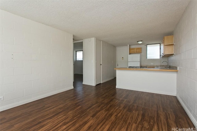 kitchen with dark wood-type flooring, freestanding refrigerator, a peninsula, light countertops, and a sink