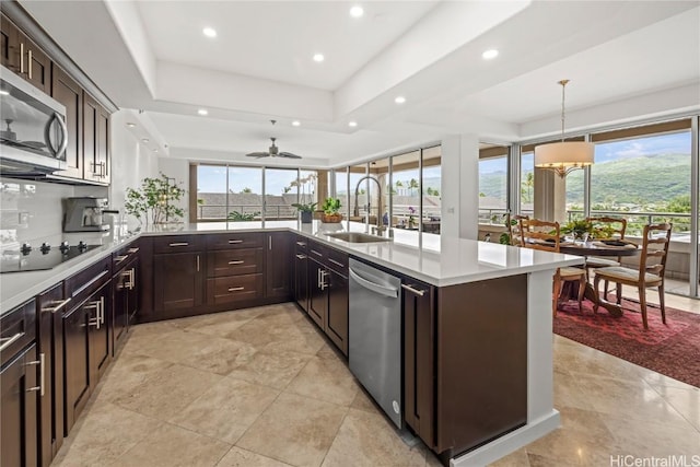 kitchen featuring stainless steel appliances, a raised ceiling, light countertops, a sink, and dark brown cabinetry