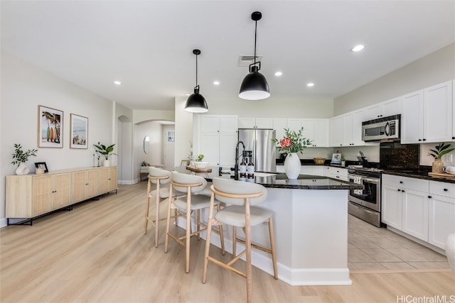 kitchen with arched walkways, visible vents, white cabinetry, appliances with stainless steel finishes, and a kitchen bar