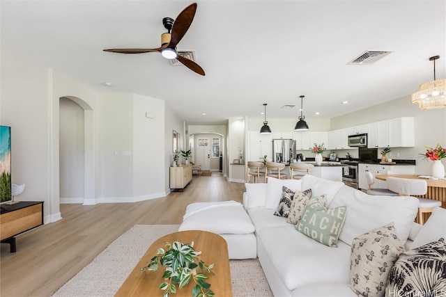 living room featuring arched walkways, recessed lighting, visible vents, light wood-style flooring, and baseboards