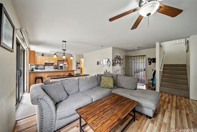 living area featuring stairs, ceiling fan, and light wood-type flooring