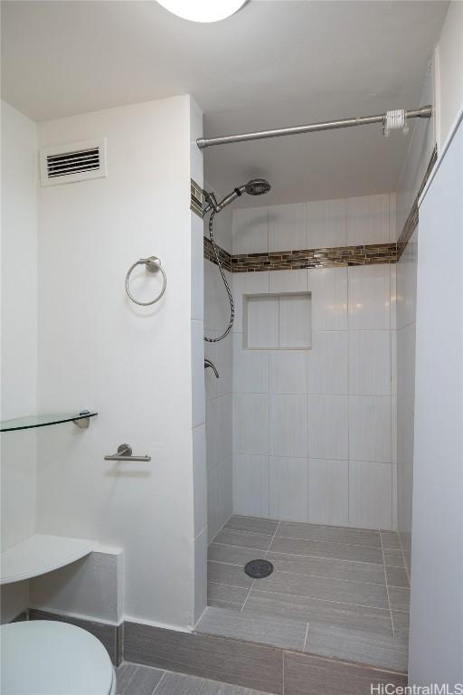 bathroom featuring visible vents, toilet, and tiled shower