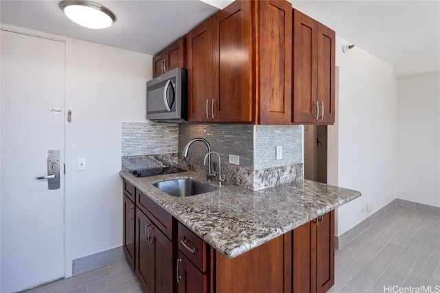 kitchen with light wood-style flooring, a sink, backsplash, light stone countertops, and stainless steel microwave