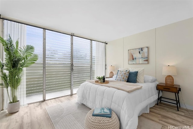 bedroom with access to exterior, light wood-style flooring, and expansive windows