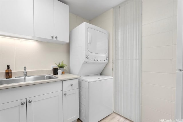 laundry area featuring a sink, cabinet space, stacked washer and dryer, and light wood finished floors