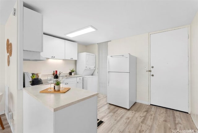 kitchen with stacked washing maching and dryer, freestanding refrigerator, light wood-style floors, white cabinets, and light countertops