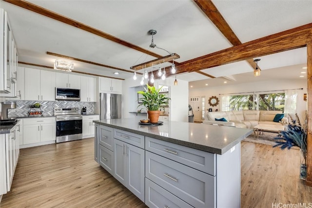 kitchen with beam ceiling, stainless steel appliances, white cabinets, light wood-style floors, and tasteful backsplash