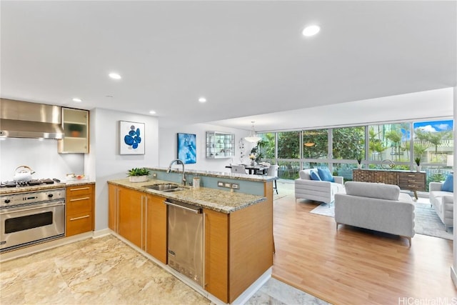 kitchen with wall chimney exhaust hood, open floor plan, a peninsula, light stone countertops, and stainless steel appliances