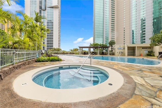 view of swimming pool featuring a city view, a pergola, fence, and a hot tub