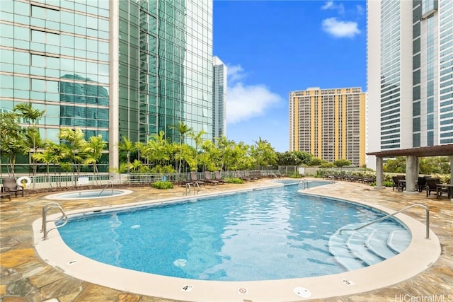 pool featuring a view of city, a patio, a hot tub, and fence