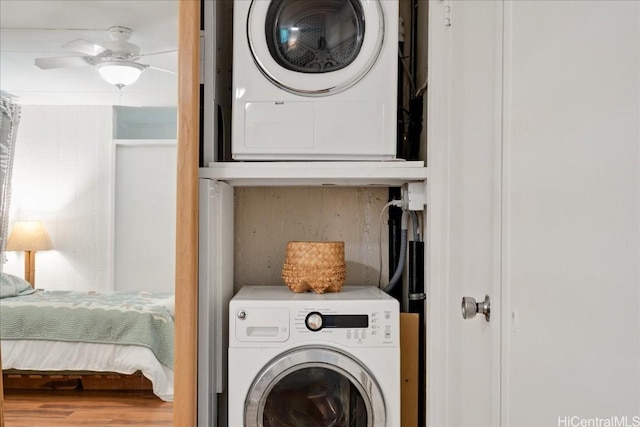 clothes washing area featuring a ceiling fan, laundry area, stacked washing maching and dryer, and wood finished floors