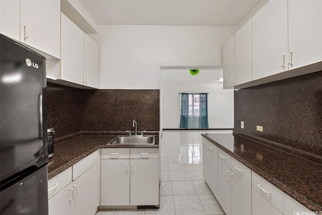kitchen with freestanding refrigerator, white cabinets, light tile patterned flooring, a sink, and decorative backsplash