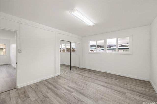 unfurnished bedroom with a closet, baseboards, and light wood-style floors