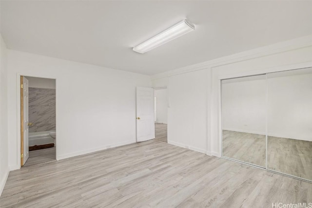 unfurnished bedroom featuring a closet, wood finished floors, and connected bathroom