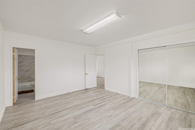 unfurnished bedroom featuring wood finished floors, ensuite bathroom, a closet, and baseboards