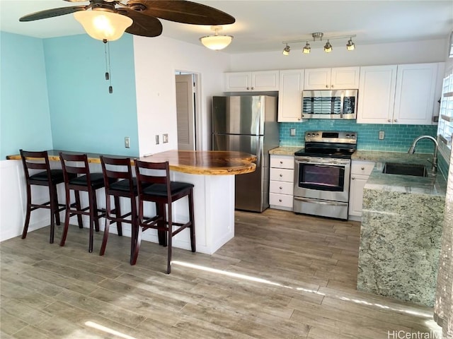 kitchen with appliances with stainless steel finishes, white cabinets, a sink, and tasteful backsplash