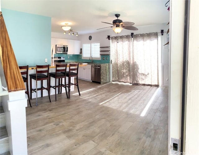 kitchen with a breakfast bar area, stainless steel appliances, white cabinetry, light wood-style floors, and backsplash