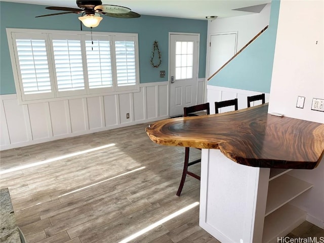 unfurnished dining area featuring a wainscoted wall, ceiling fan, wood finished floors, and a decorative wall