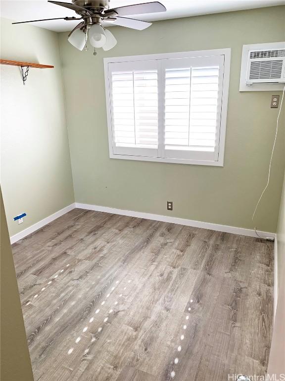 spare room featuring baseboards, a wall mounted AC, a ceiling fan, and light wood-style floors