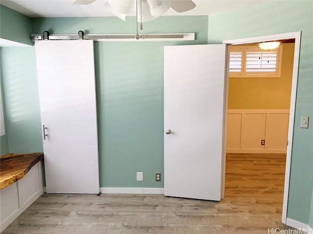 unfurnished bedroom with light wood-style flooring, a decorative wall, a ceiling fan, and wainscoting