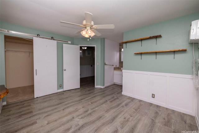 91-1016C Hoomaka St Unit 78, Ewa Beach, HI 96706 - unfurnished bedroom featuring a barn door, light wood finished floors, a wainscoted wall, ceiling fan, and a decorative wall