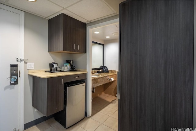 kitchen featuring a drop ceiling, light countertops, dark brown cabinets, and light tile patterned flooring