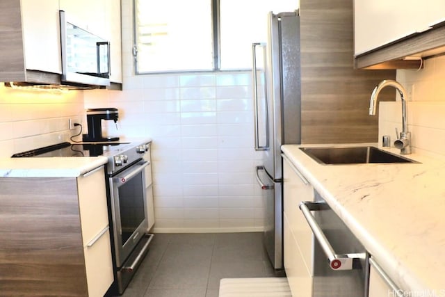 kitchen with dark tile patterned floors, a sink, white cabinetry, appliances with stainless steel finishes, and backsplash