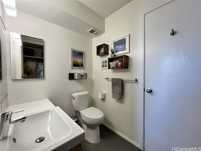 bathroom with a textured ceiling, toilet, a sink, visible vents, and baseboards