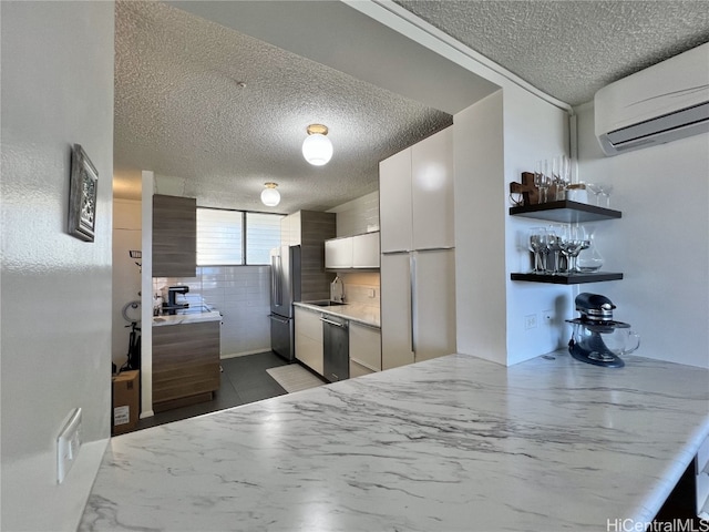 kitchen with a textured ceiling, stainless steel appliances, white cabinetry, a wall mounted AC, and modern cabinets