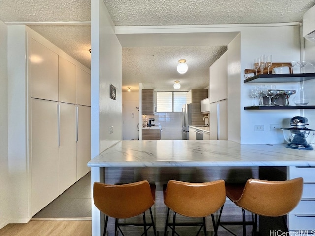 kitchen with a textured ceiling, light wood-style flooring, a sink, freestanding refrigerator, and a kitchen bar