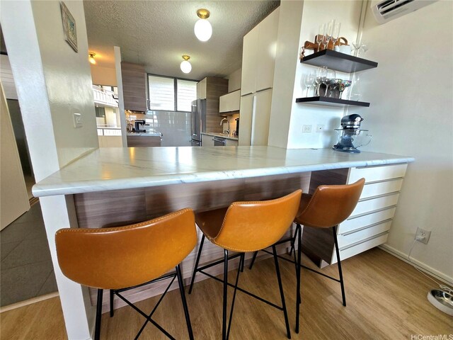 1676 Ala Moana Blvd Unit 205, Honolulu, HI 96815 - kitchen with appliances with stainless steel finishes, a peninsula, a wall mounted AC, light countertops, and a textured ceiling