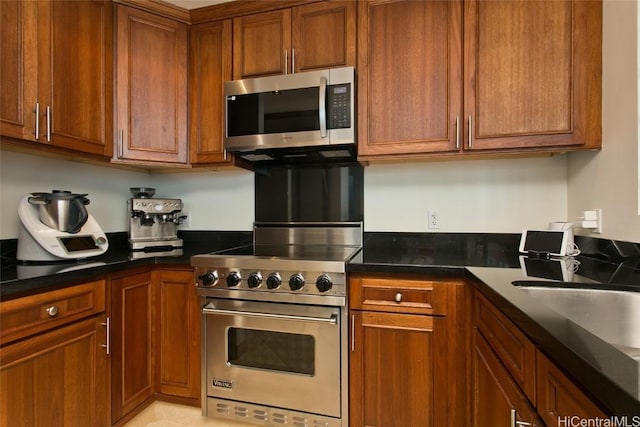 kitchen featuring stainless steel appliances, dark countertops, brown cabinets, and a sink